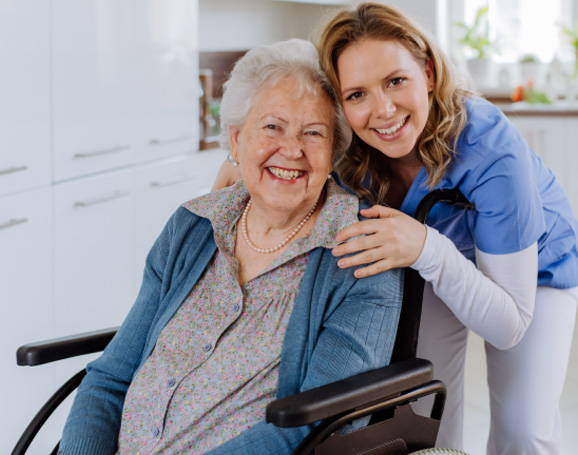 A smiling young woman and older lady in a wheelchair